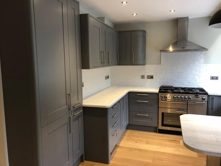 Modern kitchen with dark gray cabinetry, stainless steel appliances, white tile backsplash, and wood flooring