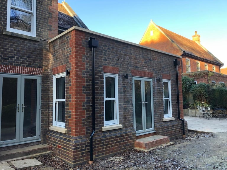 Modern brick extension on traditional brick house with large windows and patio area, golden hour lighting