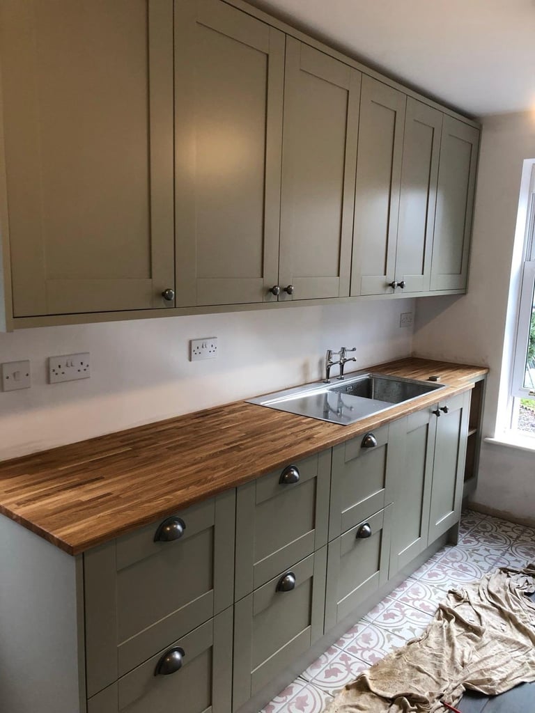 Modern kitchen with sage green cabinetry, wooden countertop, stainless steel sink, and white subway backsplash