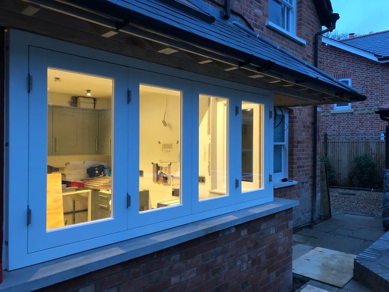 Blue modern house extension with illuminated interior showing kitchen and bathroom fixtures at dusk