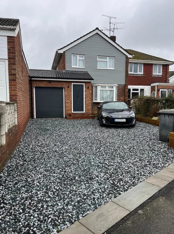 Suburban brick and gray siding house with attached garage, gravel driveway, and black car parked in front