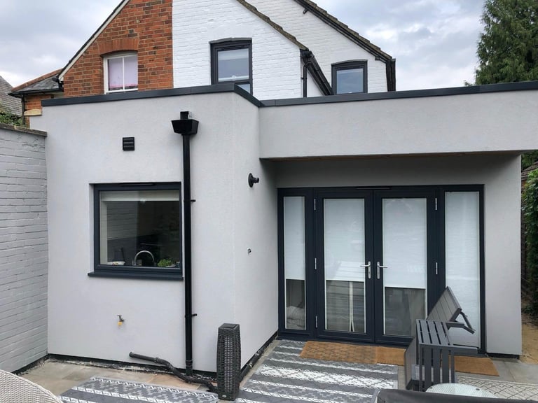 Modern white and brick house extension with black trim windows and French doors, featuring a patio area with striped rug
