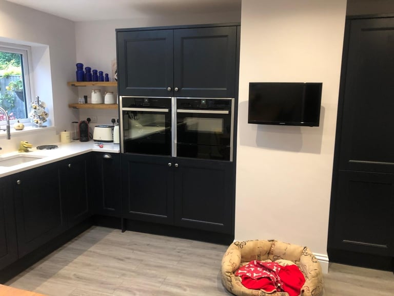Modern black kitchen with built-in ovens, wall-mounted TV, and a pet bed in the foreground