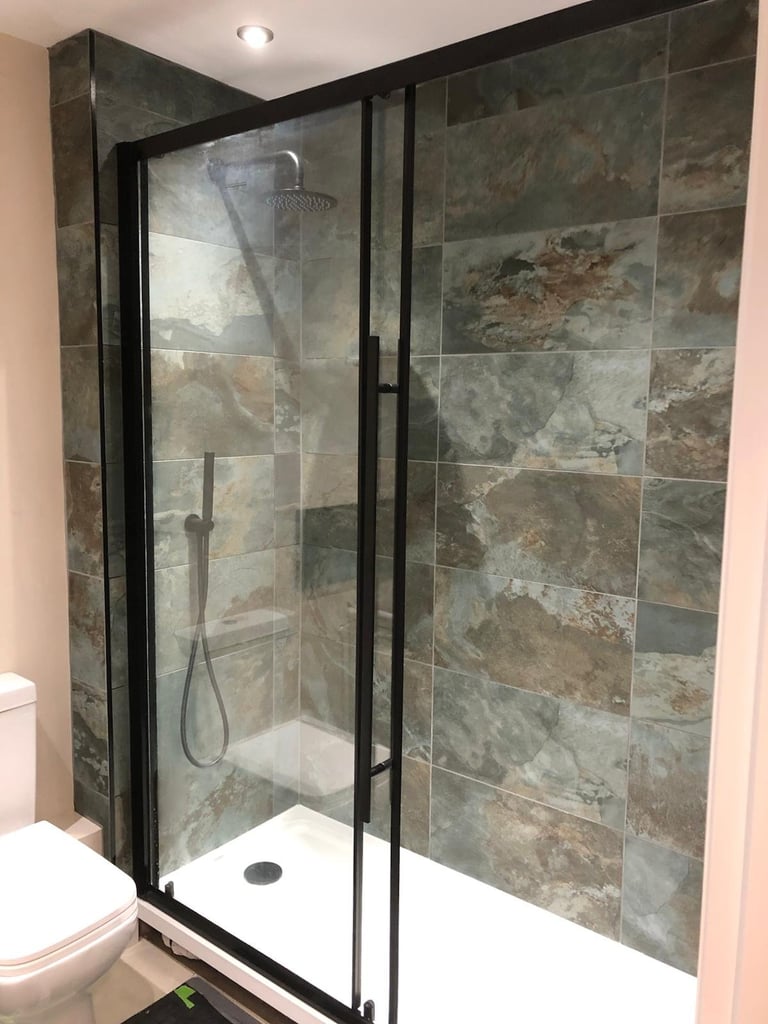 Modern bathroom shower enclosure with black frame, slate tile walls, glass doors, and white floor pan
