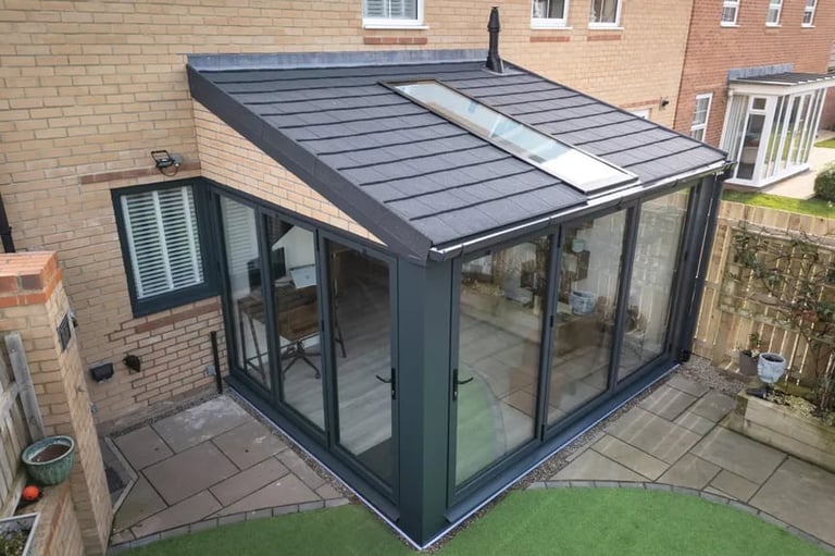 Modern glass extension with dark frame and solar panel roof attached to brick house