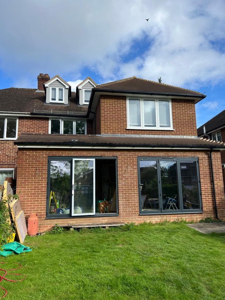 Modern brick house with large rear extension windows and manicured lawn under blue sky