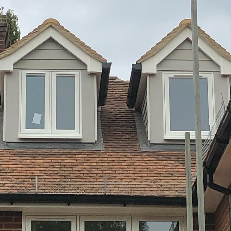 Residential brick house with two matching white dormer windows and clay tile roofing