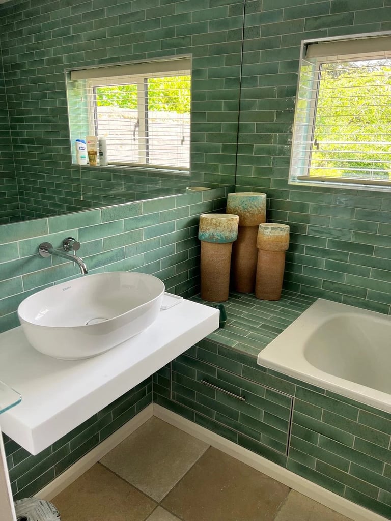 Modern bathroom with green tile walls, white vessel sink, soaking tub, and decorative woven baskets near windows