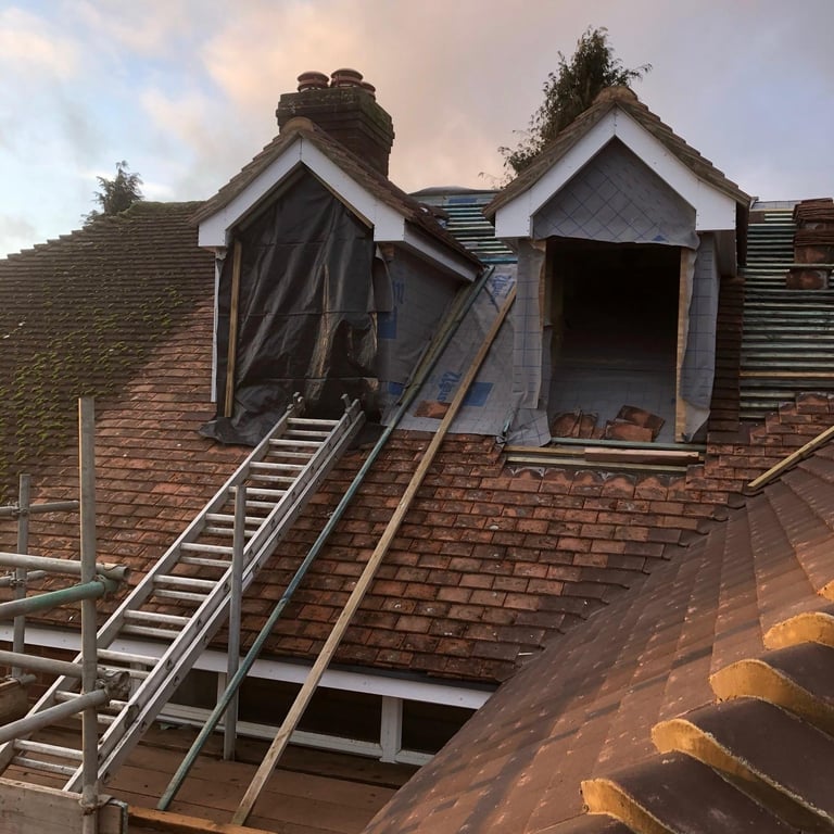 Roof renovation in progress with exposed timber framing, scaffolding, and removed roof sections on a brick building
