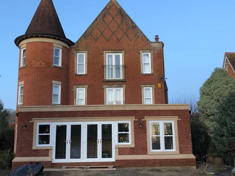 Victorian red brick building with peaked roof and turret, featuring large white-framed windows and doors on the ground level