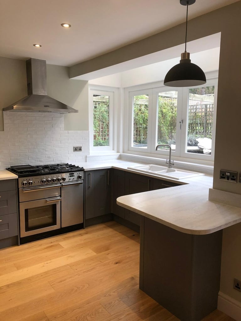 Modern kitchen with dark cabinetry, stainless steel range, white subway tile backsplash, black pendant light, and large window overlooking garden