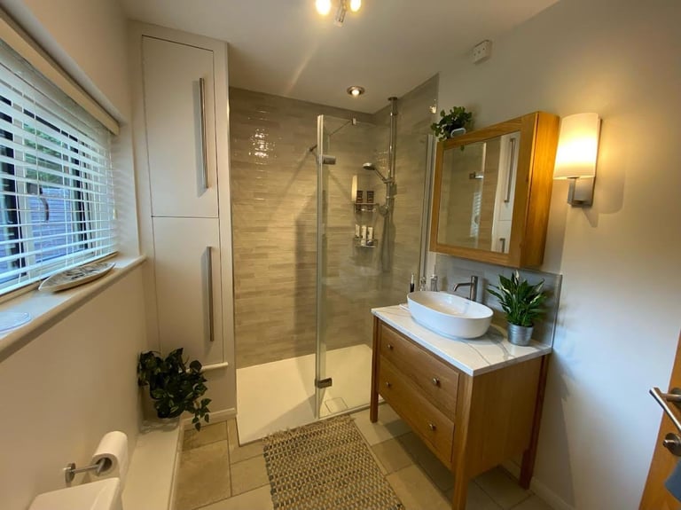 Modern bathroom with glass-enclosed shower, wooden vanity with round sink, large mirror, and neutral tile flooring