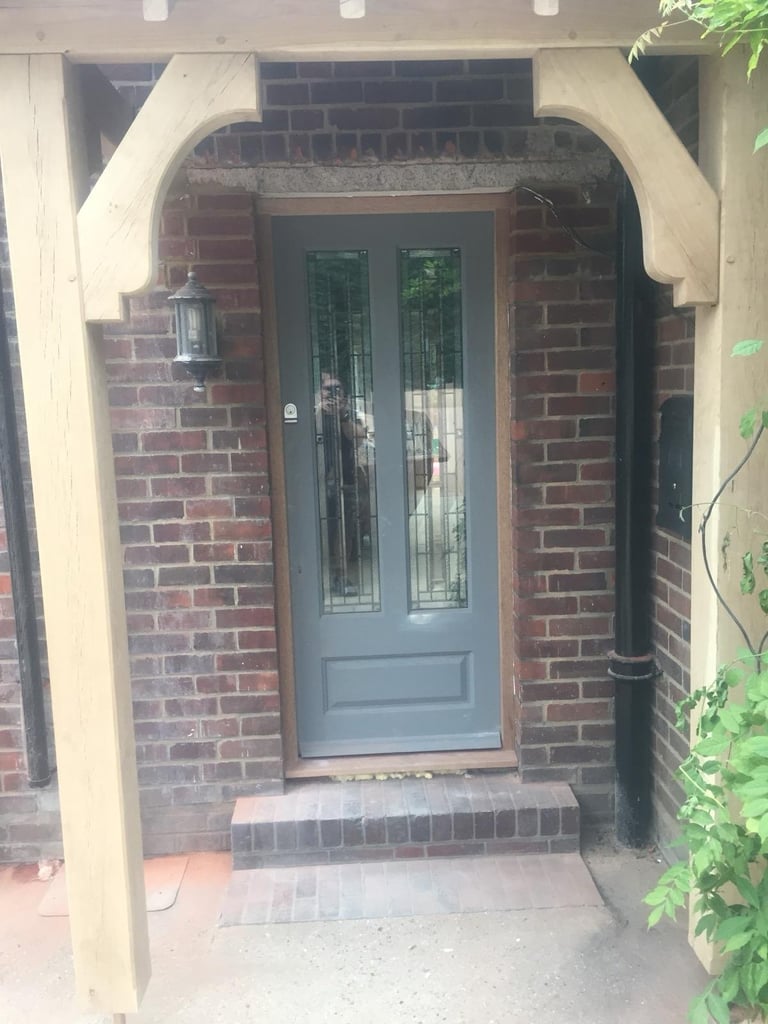 Gray front door with glass panels set in red brick archway entrance with white trim and porch steps