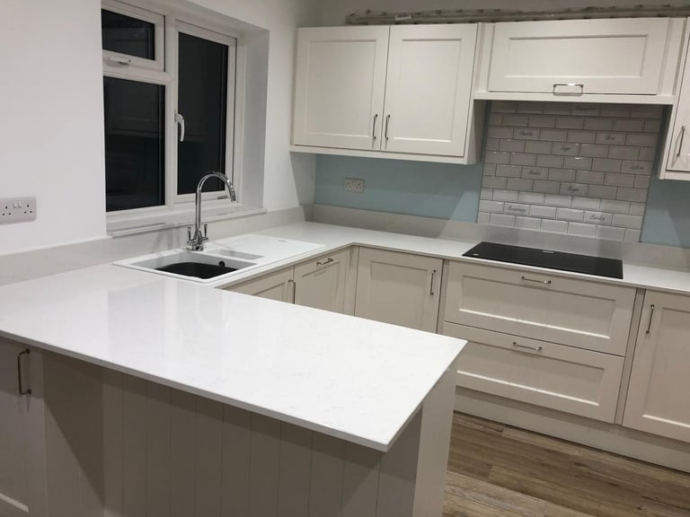 Modern kitchen with white cabinetry, island counter, gray tile backsplash, and stainless steel appliances